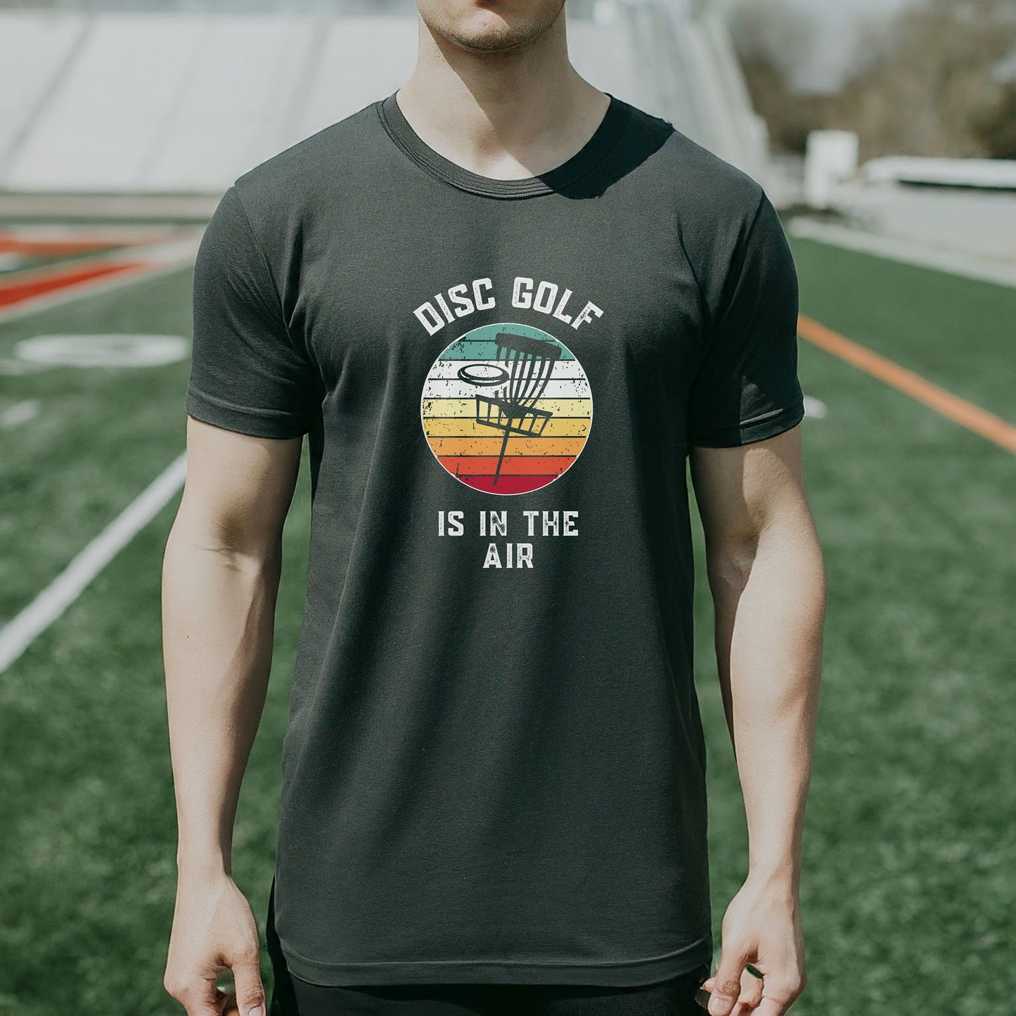 a man standing on a field wearing a disc golf is in the air shirt