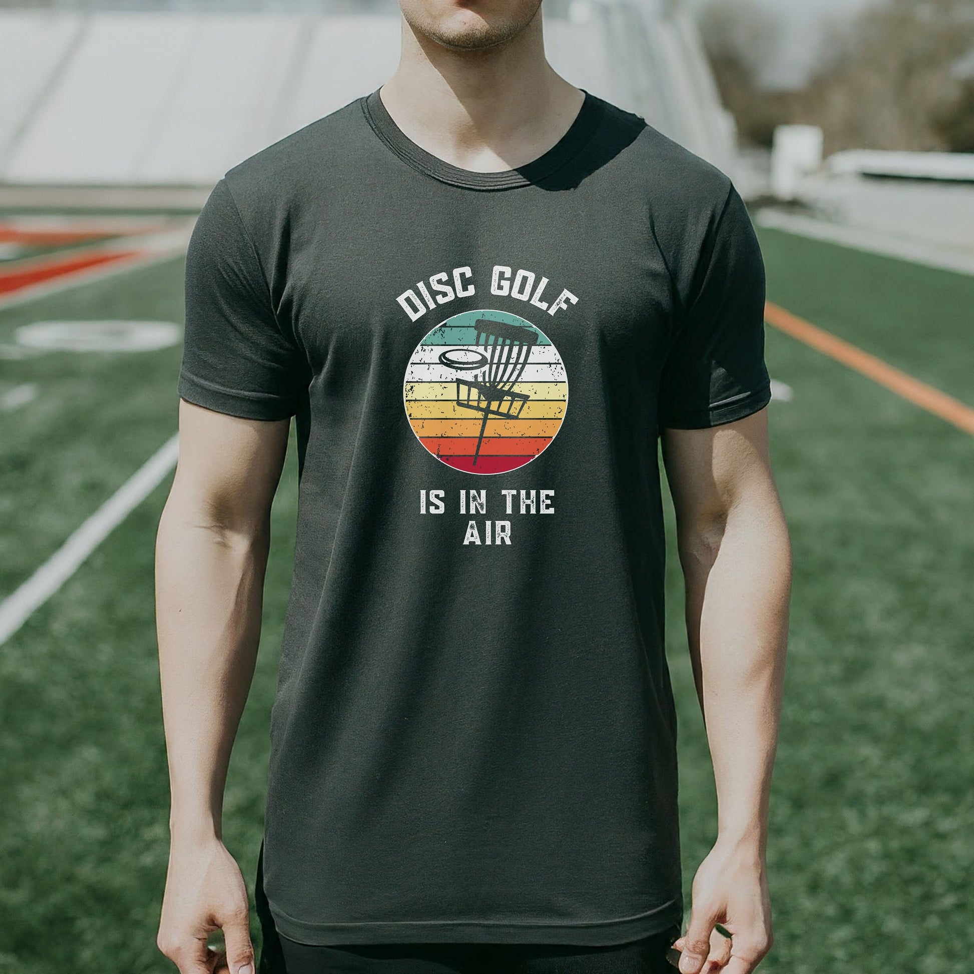 a man standing on a field wearing a disc golf is in the air shirt