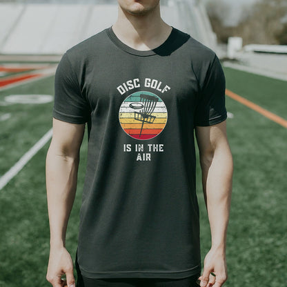 a man standing on a field wearing a disc golf is in the air shirt